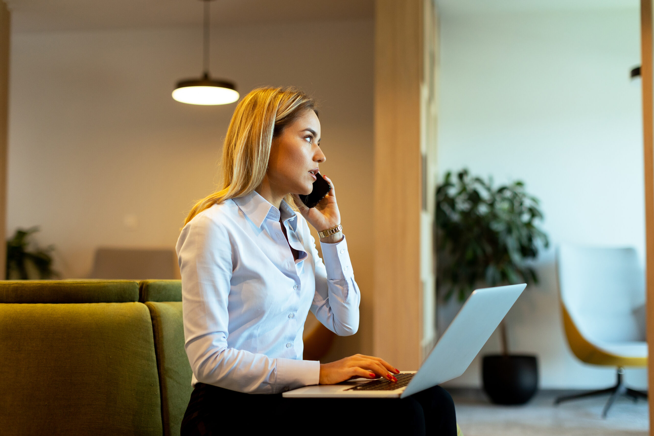 Focused professional woman multitasks efficiently, speaking on the phone and typing on her laptop in a bright, contemporary office space