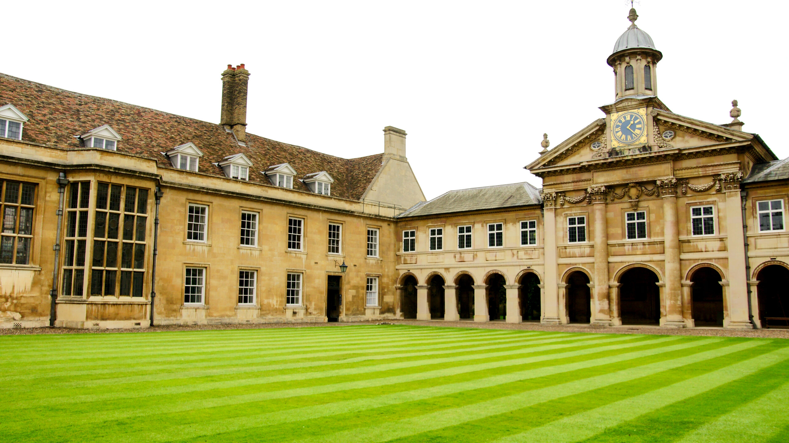 Elegant Classical College Building with Columns and Symmetry, Surrounded by Lush Green Lawn under a Cloudy English Sky in Autumn